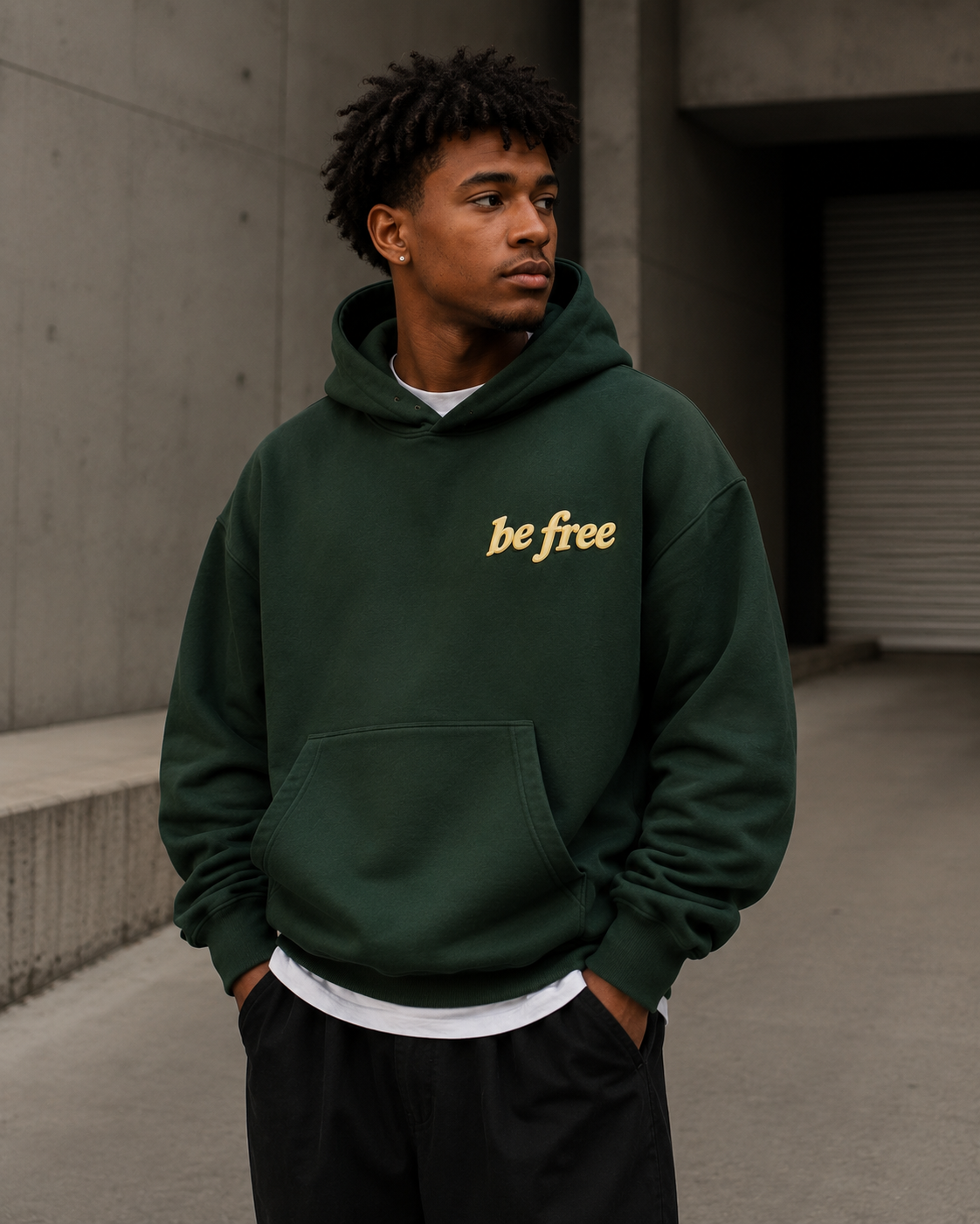 Man wearing Be Free green hoodie against concrete wall